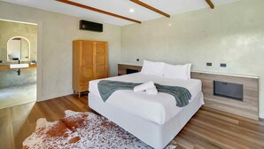 Ein modernes Schlafzimmer mit einem großen Bett, Holzbalken an der Decke, einem Holzschrank und einem Badezimmer mit Spiegel und Waschbecken.