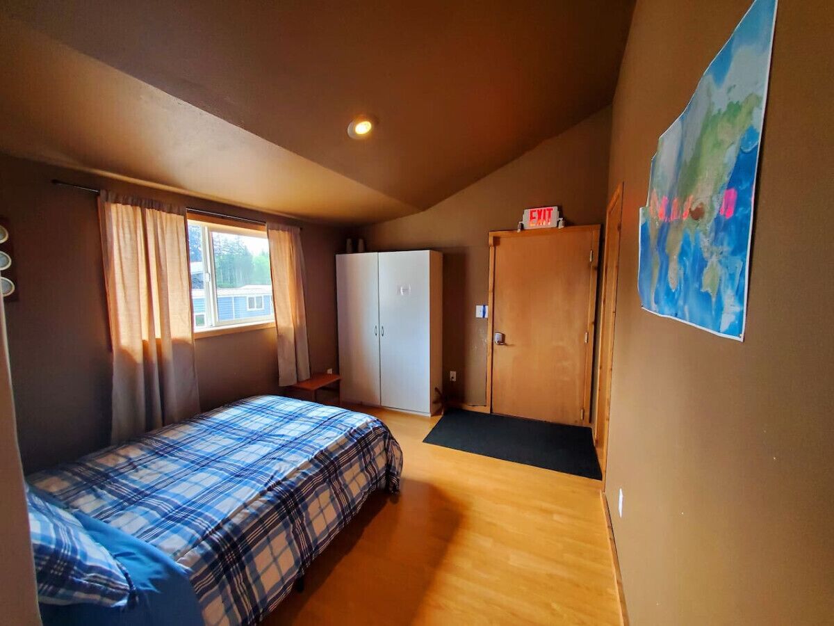 Ein Schlafzimmer mit Bett, Kleiderschrank, Tür und einem fensterbepflanzten Fenster.