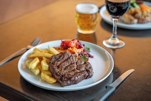 A plate with a steak, fries, and salad on a wooden table. - Discovery Resorts - Undara (Mount Surprise)