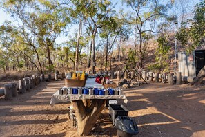 A campsite with a table set up for dining, surrounded by trees and a dirt ground. - Discovery Resorts - Undara (Mount Surprise)