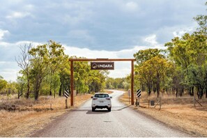 A car driving through a gate labeled "UNDARA" on a rural road surrounded by trees. - Discovery Resorts - Undara (Mount Surprise)