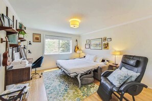 Une chambre à coucher avec un lit, une chaise, un bureau, des étagères remplies de livres et une guitare, ainsi qu’une fenêtre.