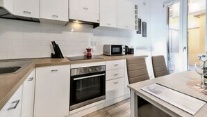 A modern kitchen with white cabinets, a built-in oven, a microwave, and a dining area with a table and chairs. - Wine Apartments Florence Bardolino (Firenze)