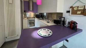 Cozinha moderna com armários brancos, bancada roxa, fogão a gás, micro-ondas, cafeteira e um eletrodoméstico vermelho na bancada.