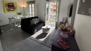 Uma sala de estar moderna com um sofá preto, mesa de centro branca e uma área de jantar com mesa e cadeiras brancas.