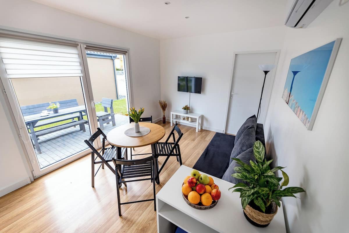 A modern living room with a round table, black chairs, a sofa, a TV, and a balcony with outdoor furniture.