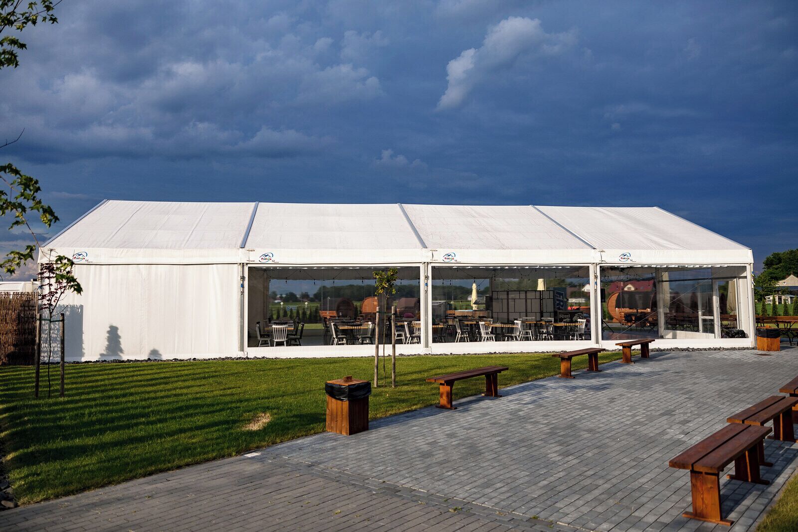 Ein großes weißes Zelt mit überdachter Terrasse, Sitzgelegenheiten im Freien und einem Rasenplatz.