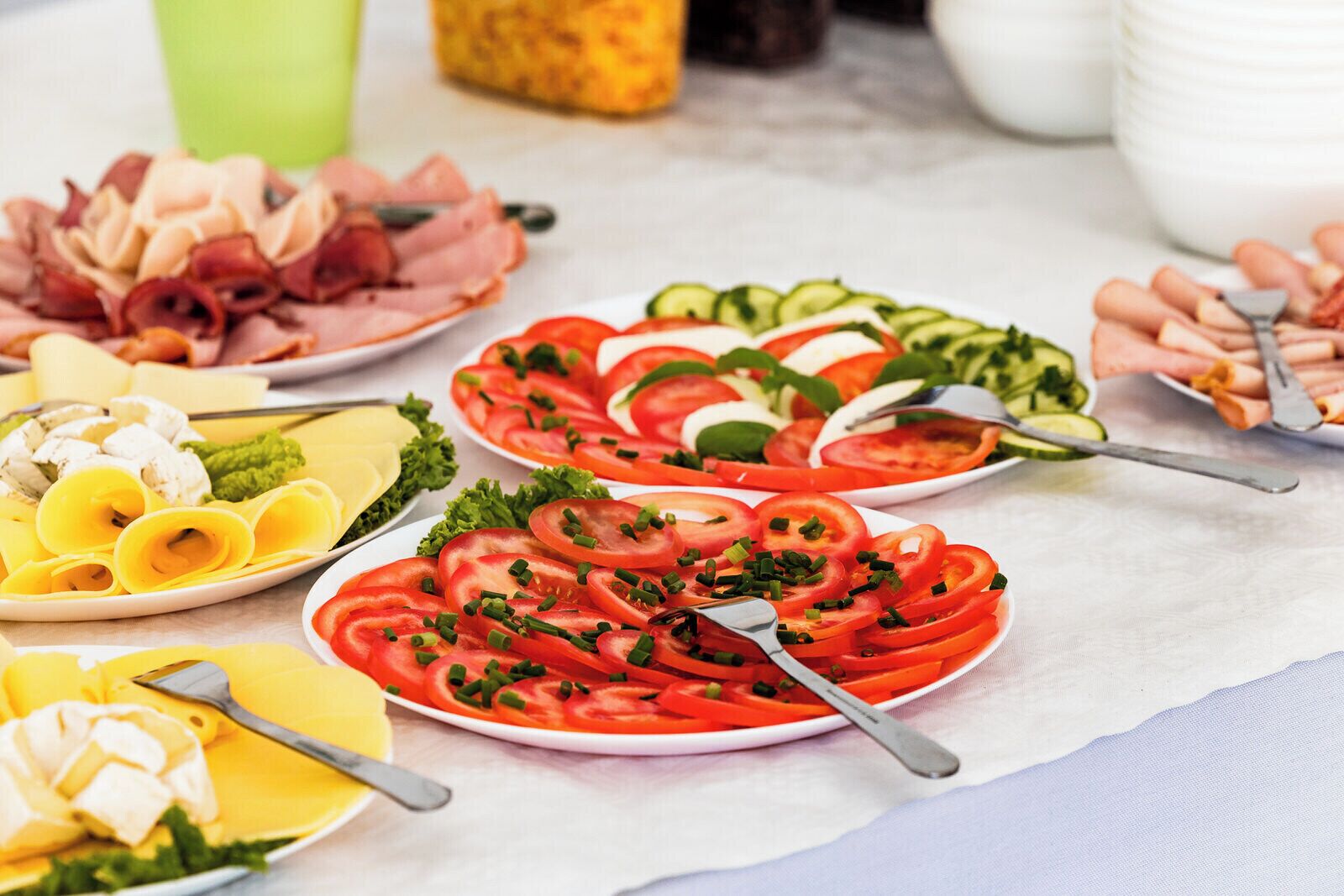 Une variété d’aliments sont disposés sur une table, notamment des tomates et des concombres coupés en tranches, ainsi que du fromage.