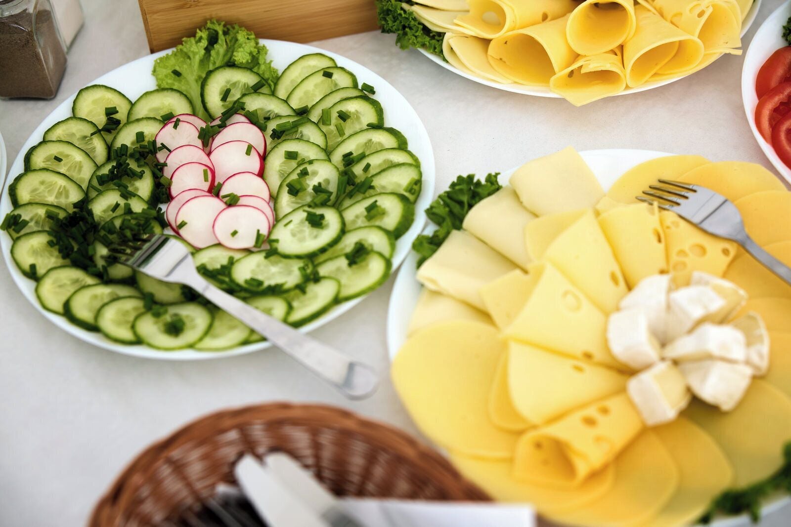 A table with various food items including sliced cucumbers, radishes, cheese, and a fork.