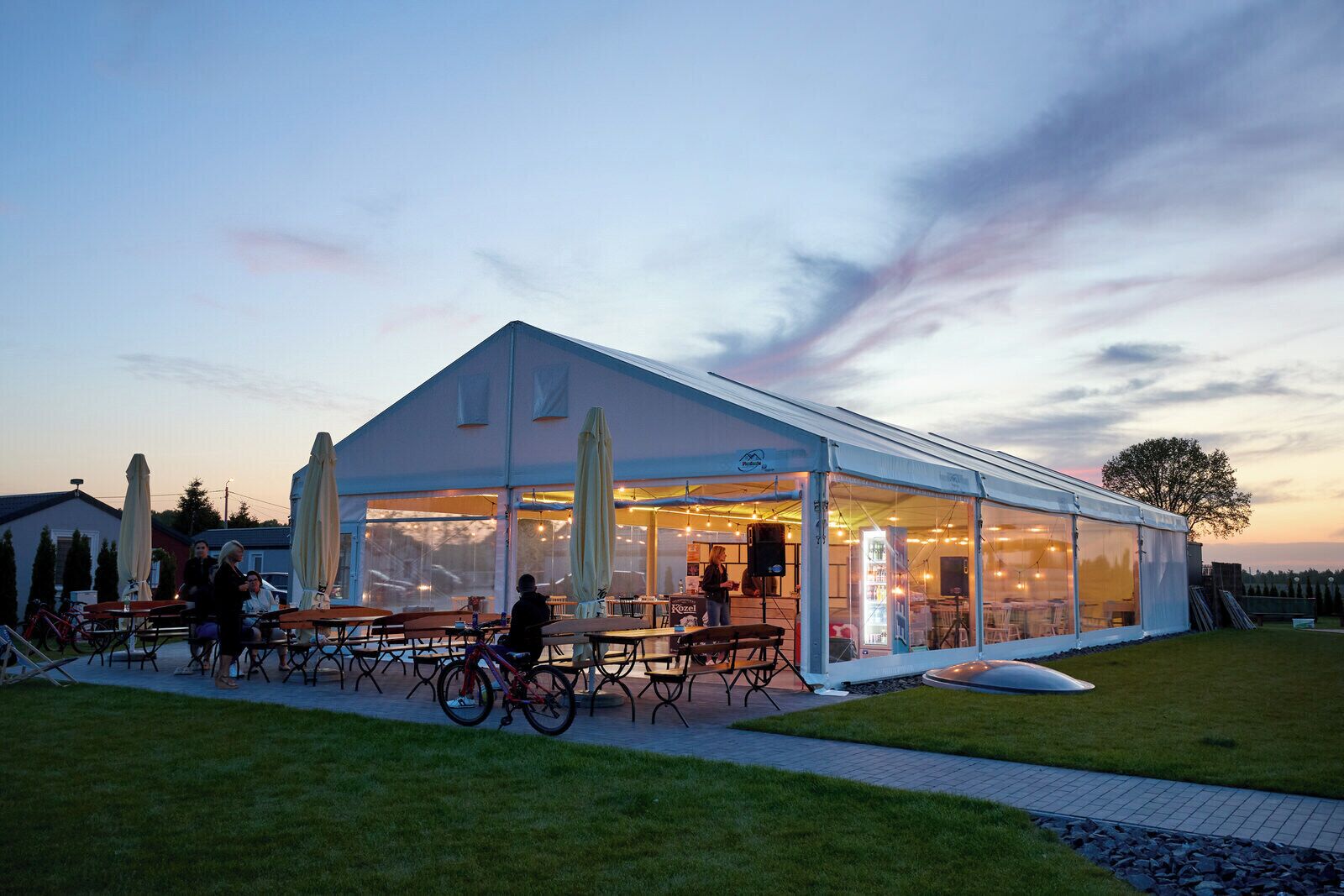 A covered outdoor seating area with tables and chairs, a bicycle, and a grassy lawn.