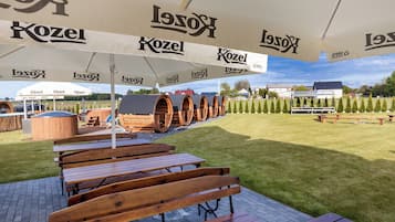 Un área de estar al aire libre con bancos y mesas de madera bajo grandes sombrillas blancas con el logo de 'Kozel'.