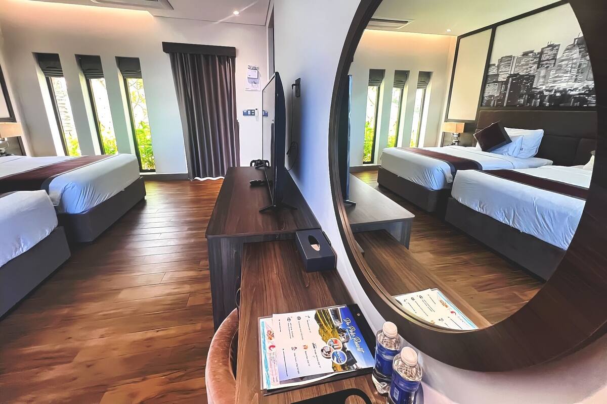 A modern hotel room with a large mirror, two beds, a desk, and a view of greenery through large windows.