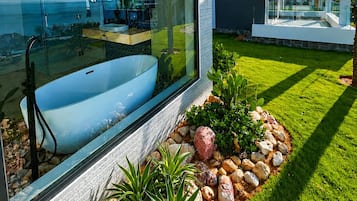 Una casa moderna con un amplio ventanal, una bañera y un jardín bien cuidado.