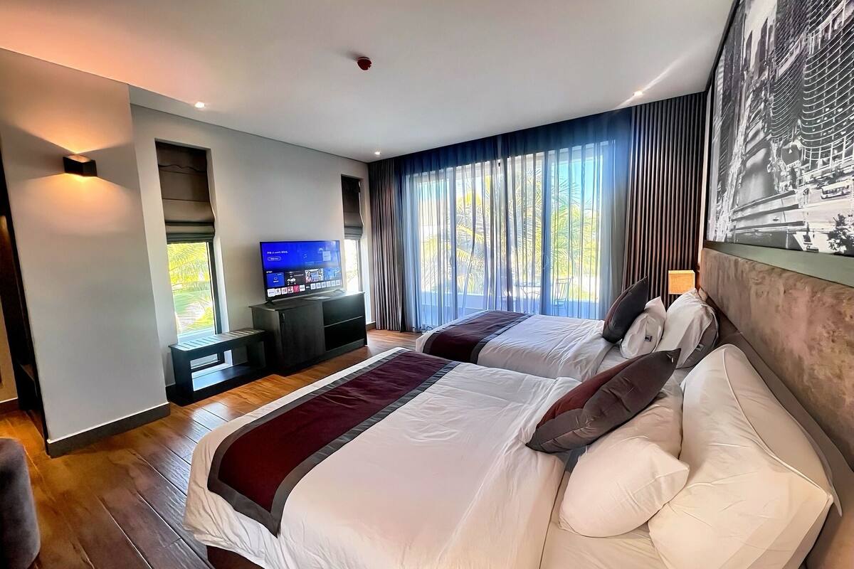 A modern hotel room with two beds, a TV, and a balcony with curtains.