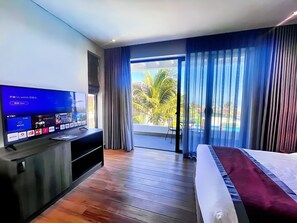 A hotel room with a TV displaying a webOS interface, a bed with a white and maroon bedspread, a wooden floor, and a view of palm trees and a pool through the window. - Du Parc Resort Mũi Né (Mui Ne)
