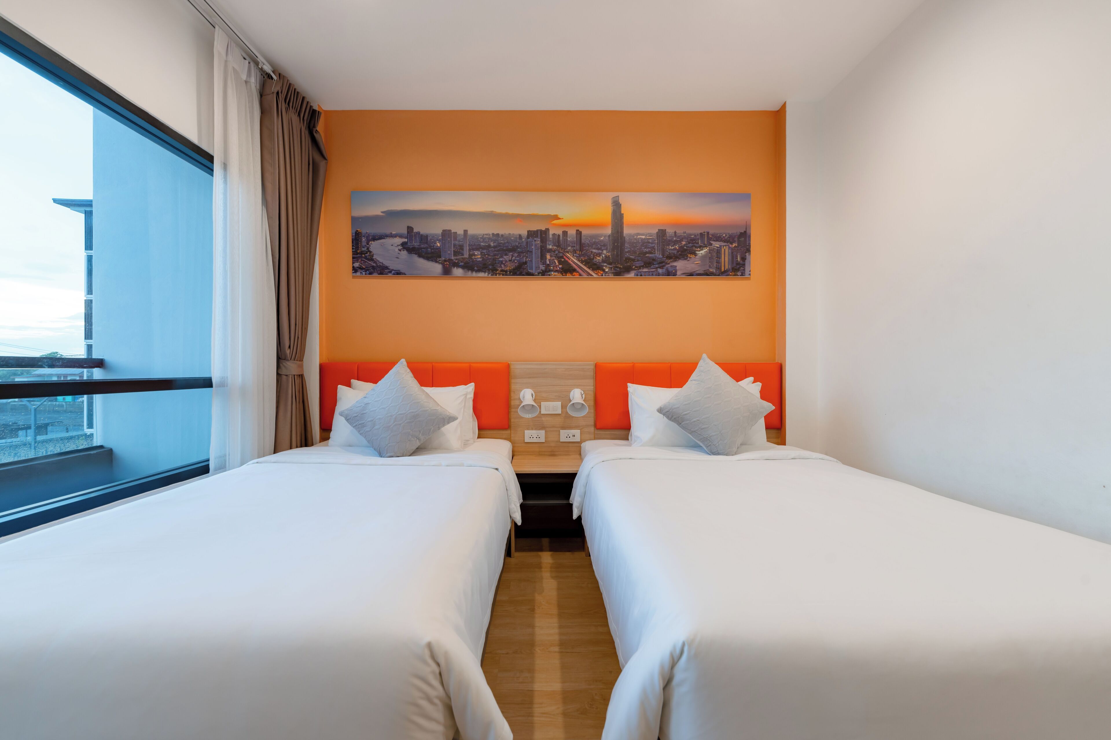 Hotelkamer met twee bedden, een stadslandschap aan de muur en uitzicht op de stad.