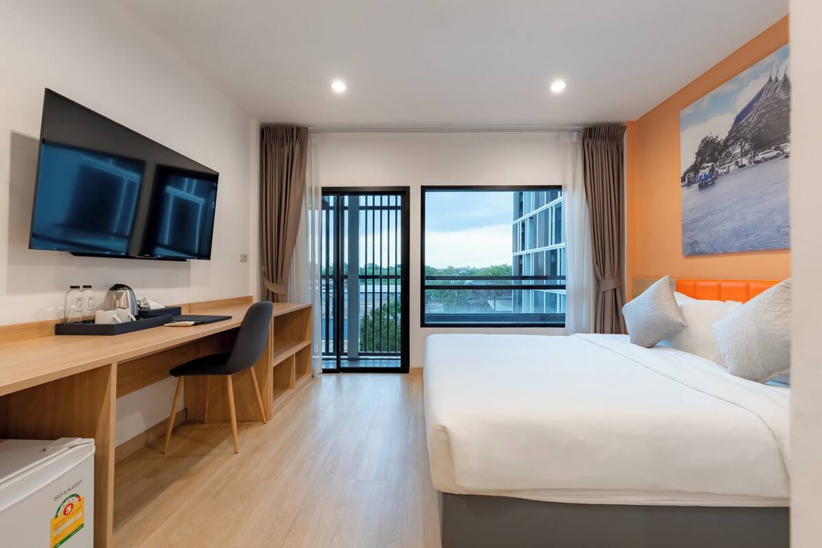 Une chambre d’hôtel comprenant un lit, un bureau avec une chaise, une télévision, une fenêtre donnant sur un paysage agréable et une porte menant à un espace extérieur.