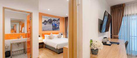Habitación de hotel con cama, escritorio con planta, televisor y baño con pared de acento naranja.