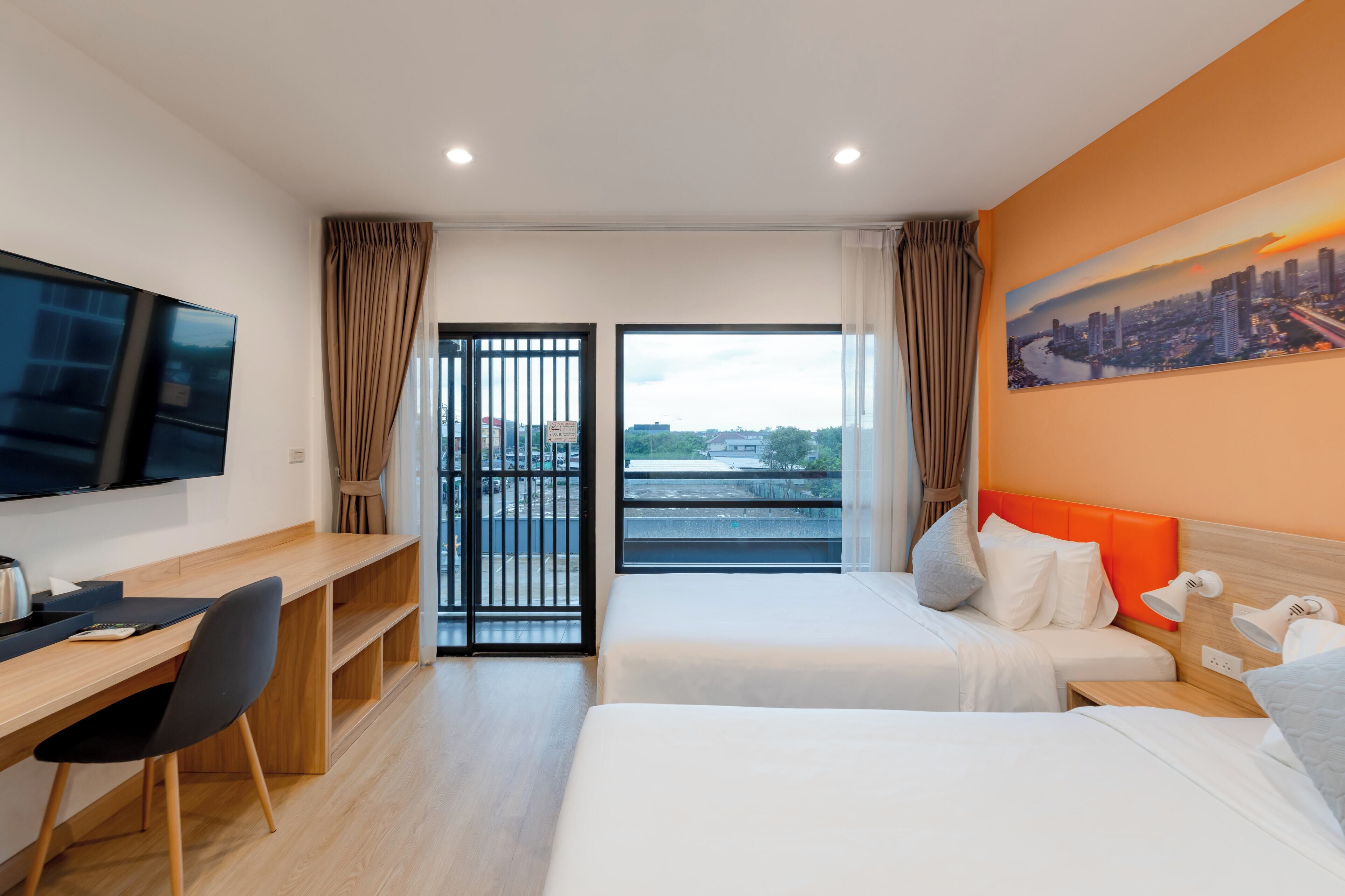 Habitación de hotel con cama, escritorio, silla, televisor y vista panorámica de la ciudad.