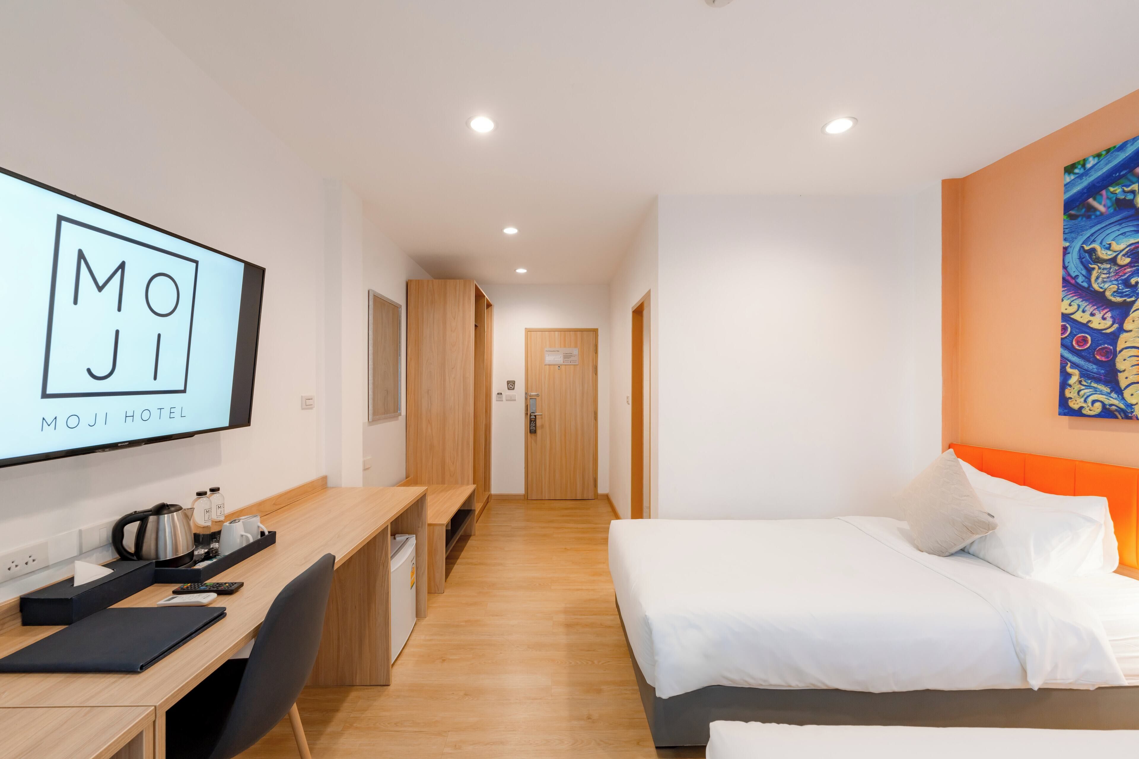 A hotel room with a bed, desk, and a TV displaying "MOJI HOTEL".