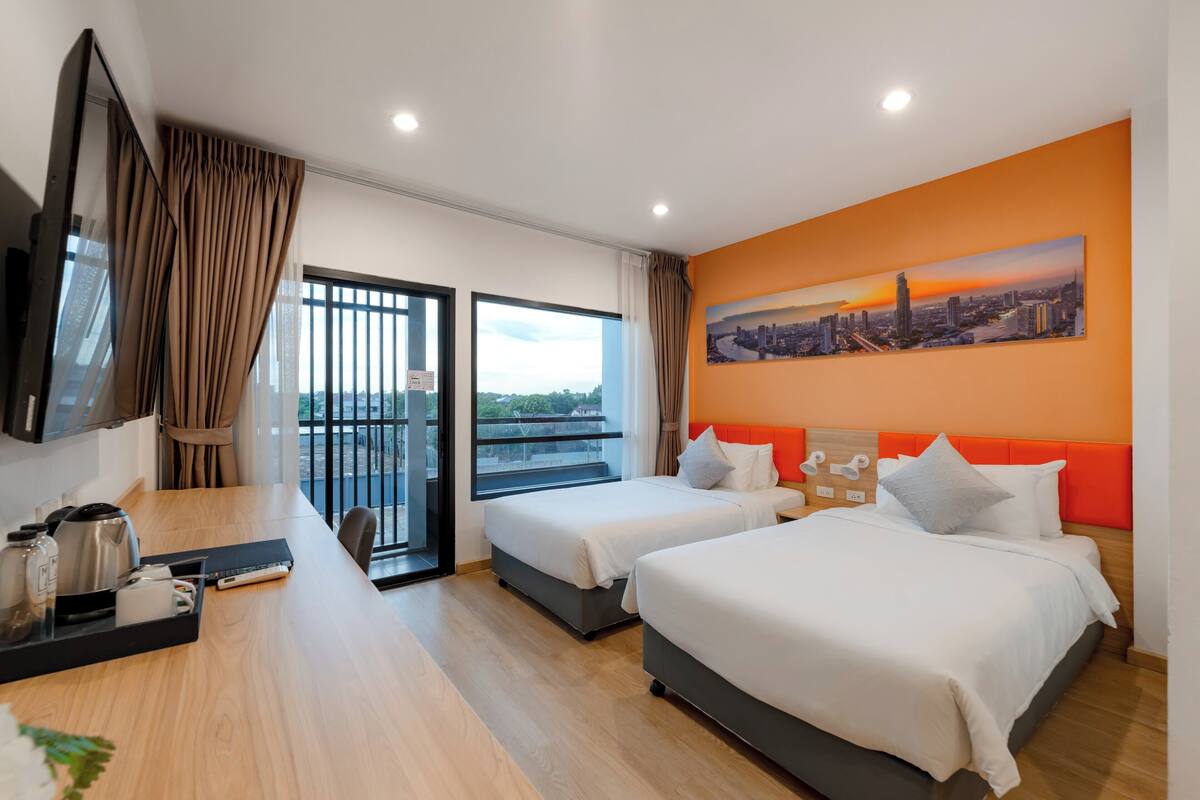 Une chambre d’hôtel avec deux lits, un bureau avec une télévision et un tableau représentant un paysage urbain accroché au mur.