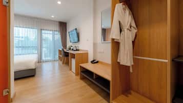 A hotel room with a bed, a desk, a TV, a robe hanging, and a wooden wardrobe.