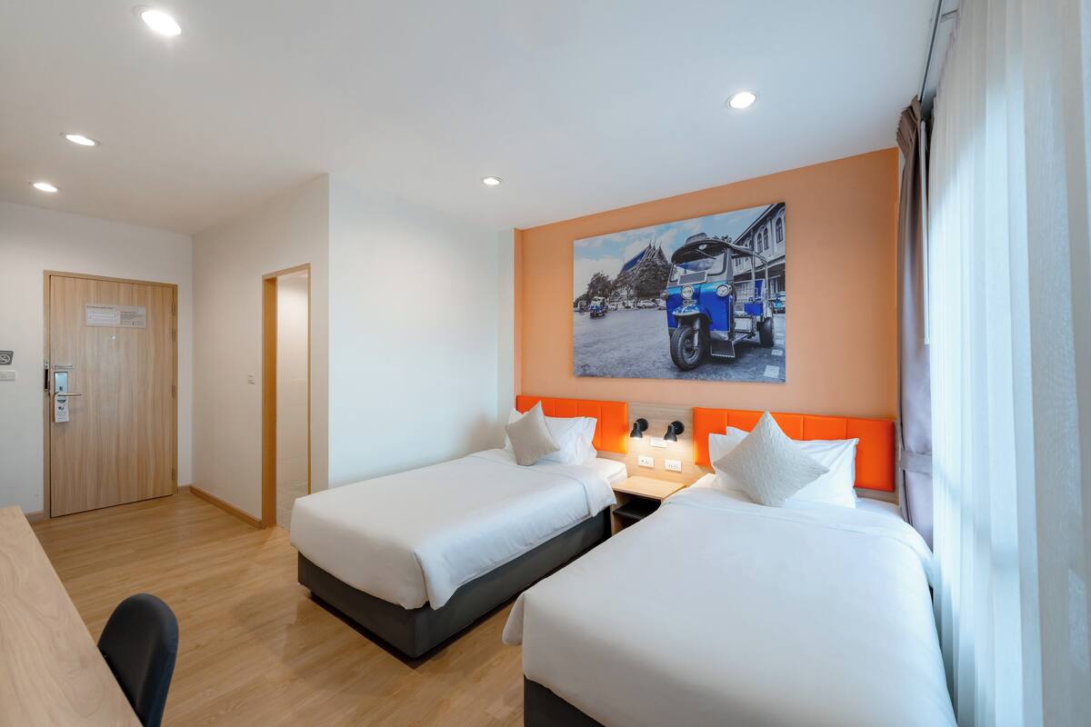 Une chambre d’hôtel avec deux lits, un bureau et un tableau représentant un camion bleu accroché au mur.