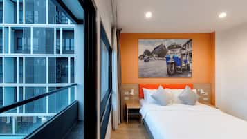 Una habitación de hotel con una cama, una mesita de noche, una lámpara de pared y un ventanal con vistas a un edificio.