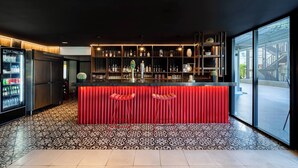 Een moderne bar met een rode aanrecht, planken met flessen en een patroon vloer.