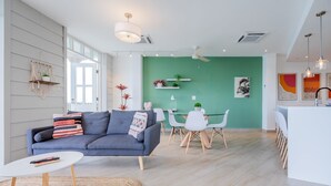 Ein modernes Wohnzimmer mit einem grauen Sofa, einem kleinen runden Tisch und einem Essbereich mit weißem Tisch und Stühlen.