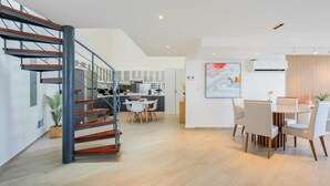 Un interior moderno con una escalera, cocina, comedor y sala de estar con un gran ventanal.