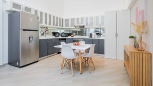 Una cocina moderna con armarios blancos, un refrigerador de acero inoxidable, una mesa de comedor con sillas y un aparador de madera con un florero.