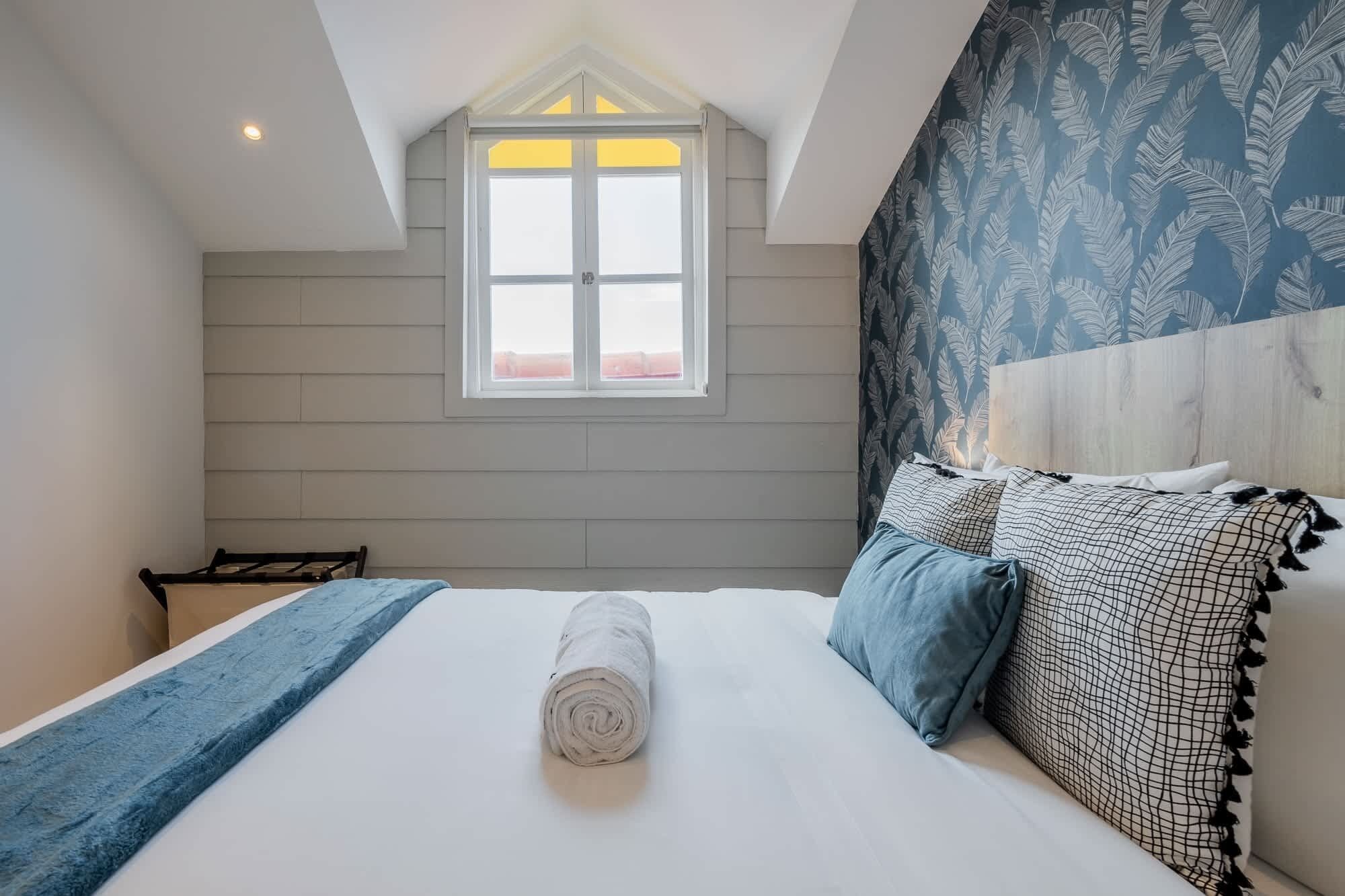 Une chambre à coucher avec un lit, une fenêtre et une tête de lit ornée d’un motif de feuilles.