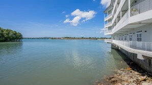 Un hotel frente al agua con varios balcones, una vista despejada del agua y un puente distante.