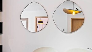 Ein modernes Schlafzimmer mit einem Bett, zwei weißen Stühlen, einem kleinen Tisch mit Kerzen und zwei Wandspiegeln.