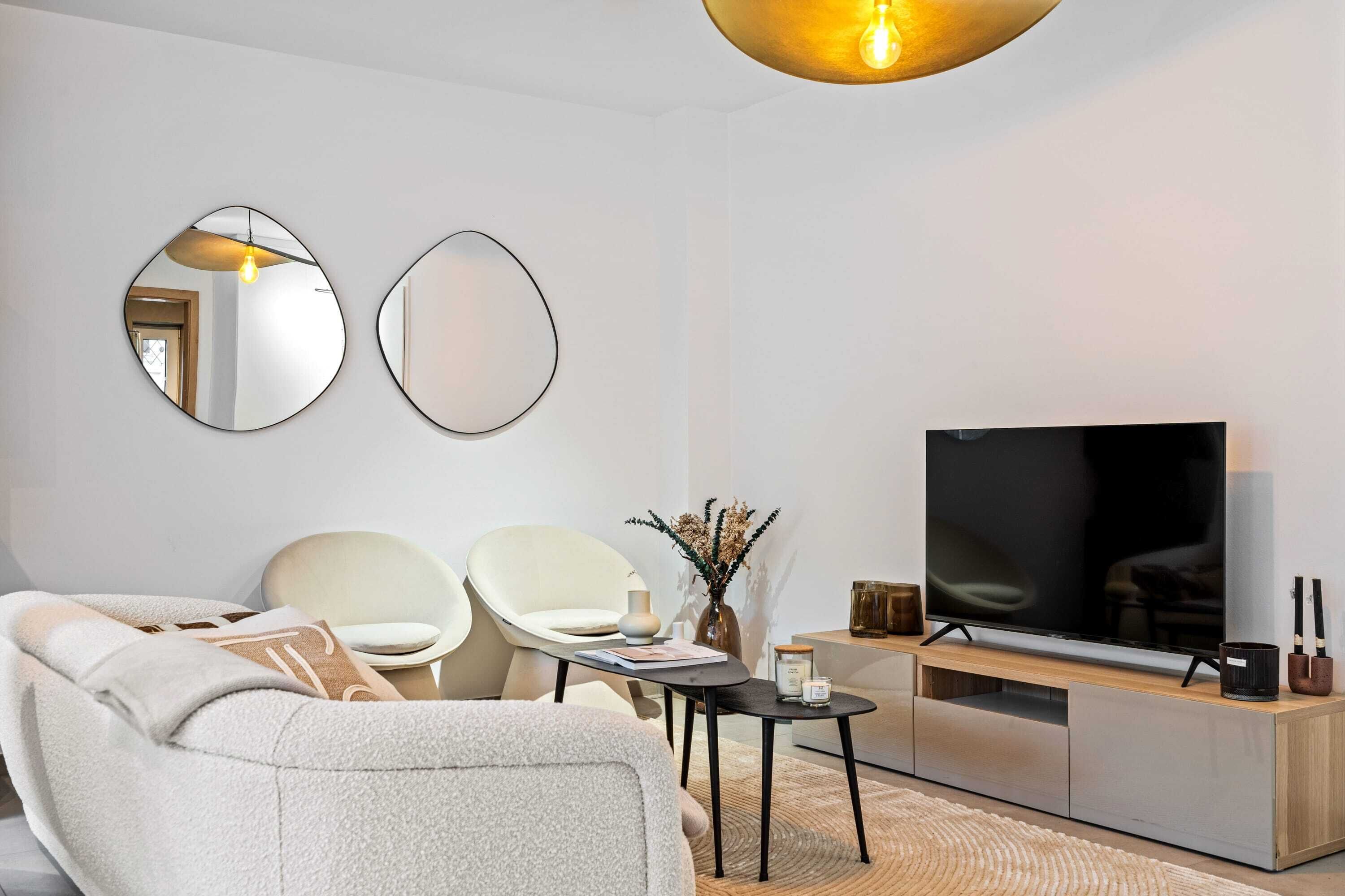 Un salon moderne comprenant un canapé, deux fauteuils, une table basse, un téléviseur et un miroir décoratif.