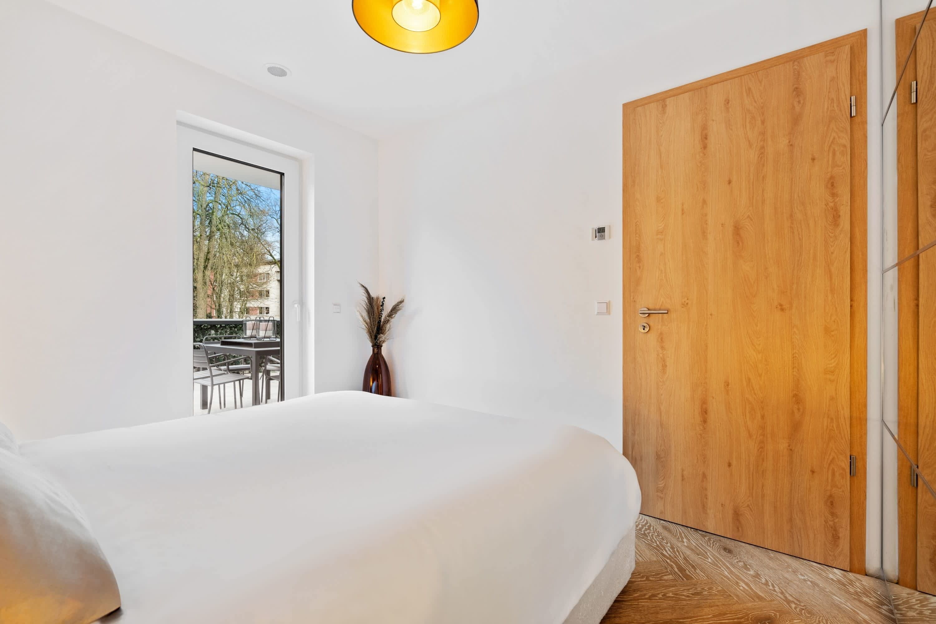 A bedroom with a large bed, a wooden wardrobe, and a window with a view of the outside.
