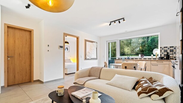 Ein modernes Wohnzimmer mit Sofa, Couchtisch und Blick auf Küche und Garten.
