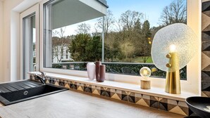 Eine moderne Küche mit einem schwarzen Spülbecken, einem Fenster mit Blick auf Bäume und Dekorationen an der Fensterbank.