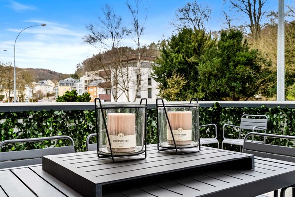 A table with two candles labeled "Jardin Deden" on a balcony with a view of buildings and trees.