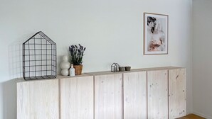 A wooden panel wall with a framed picture, a wire shelf with decorative items, and a potted plant. - Beautiful House Skanör - Falsterbo (Skanör)