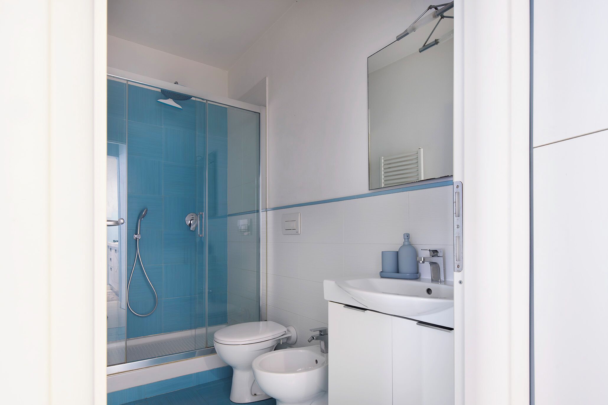 Une salle de bain moderne avec une douche à parois de verre, des toilettes blanches et un lavabo avec un miroir au-dessus.