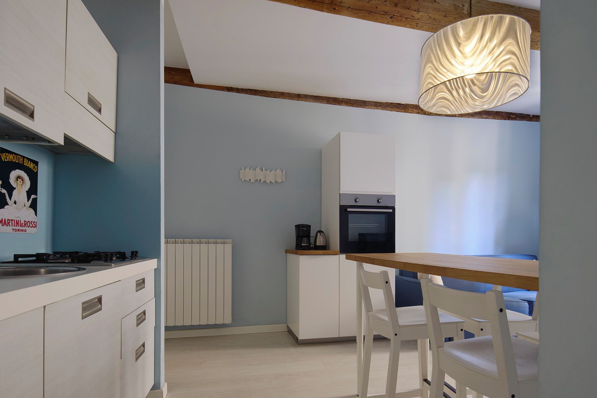 Une cuisine moderne avec des meubles blancs, une table en bois et un luminaire suspendu.