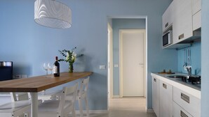 Una cocina moderna con una mesa de madera, sillas blancas, una lámpara colgante y una puerta que da a otra habitación.
