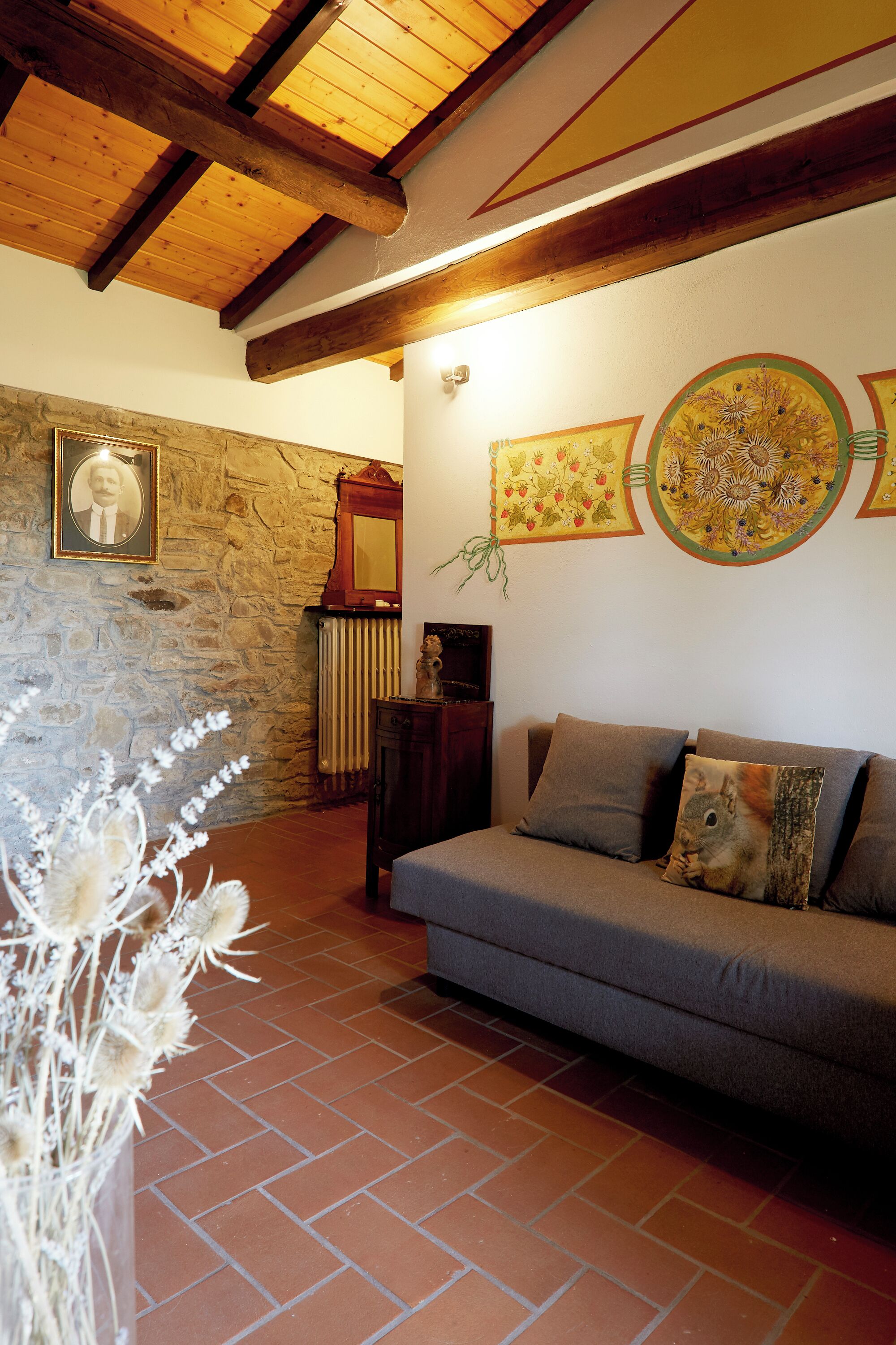 Uma sala de estar aconchegante com parede de pedra, teto de madeira e sofá cinza com almofadas decorativas.