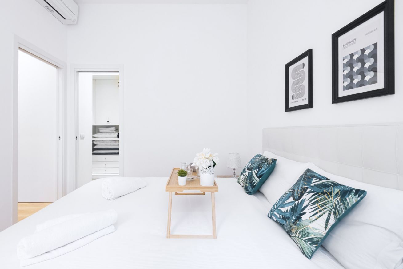 Ein modernes Schlafzimmer mit einem ordentlich bezogenen Bett, einem Nachttisch mit Pflanze und zwei gerahmten Bildern an der Wand.