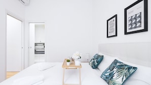 Une chambre à coucher moderne avec un lit soigneusement fait, une table de chevet ornée d’une plante et deux tableaux encadrés accrochés au mur.