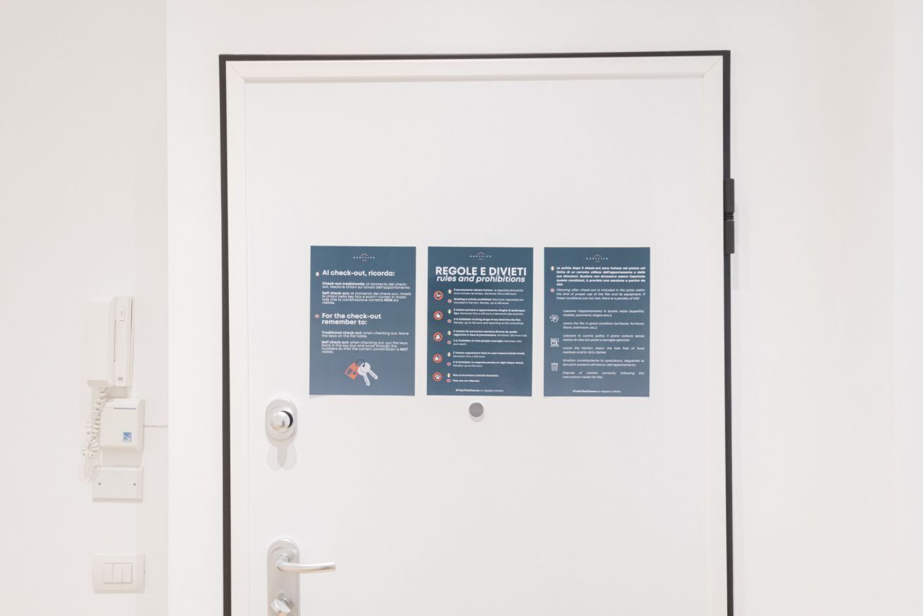 A door with three informational signs: 'AI check-out, ricorda: For the check-out remember to...', 'REGOLE E DIVIETI rules and prohibitions', and 'REGOLE E DIVIETI rules and prohibitions'.