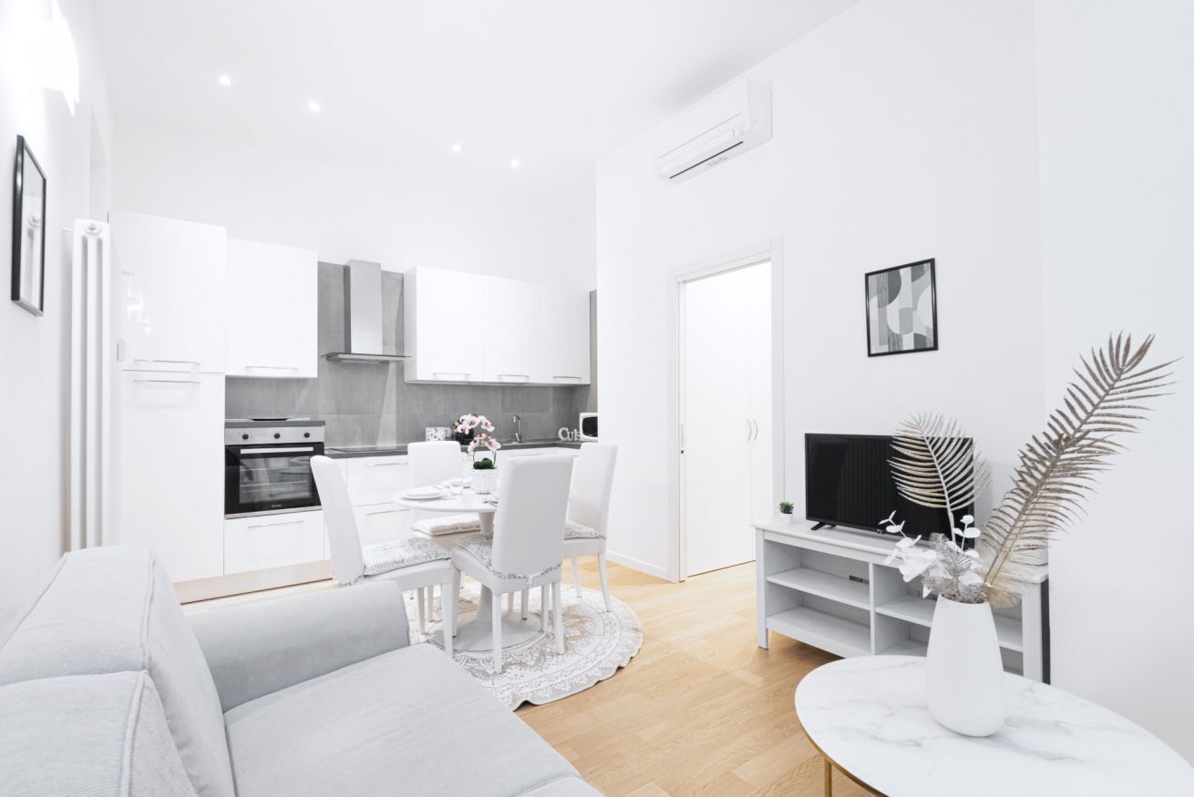 A modern, white-themed living room with a sofa, a dining area with chairs and a table, and a kitchen in the background.