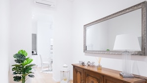Un couloir avec une armoire en bois, un grand miroir, une plante en pot et une chaise blanche.